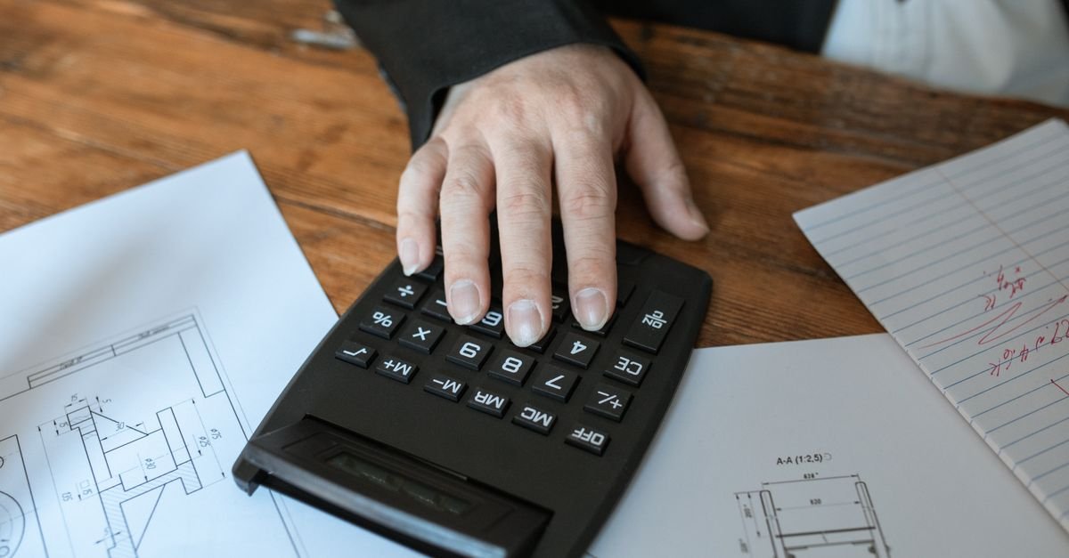 Gros plan sur des mains utilisant une calculatrice posée à côté de documents chiffrés